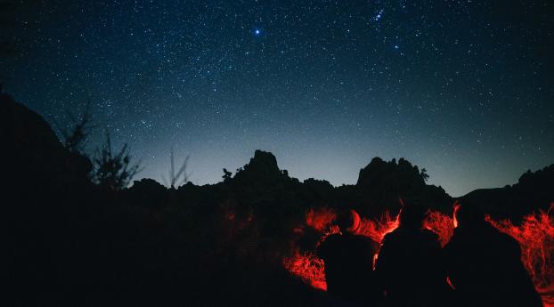 People Sitting Around Campfire In Dark Night Wallpaper